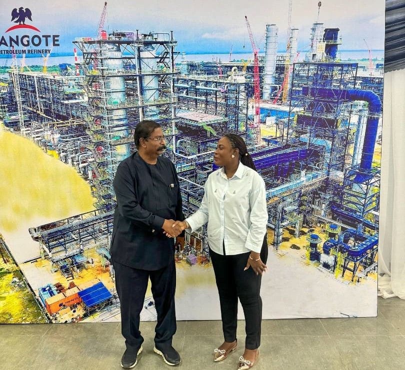 Two people shake hands in front of the refinery's processing units on a visit to the Dangote Petroleum Refinery, Lagos, 2024