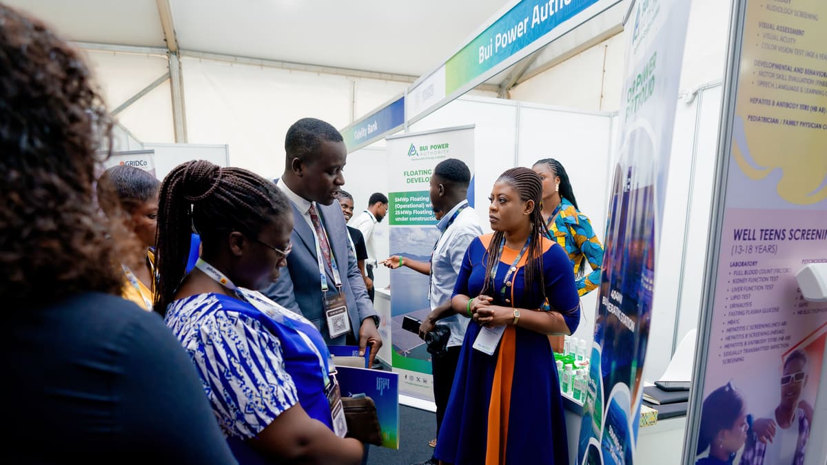 At the Bui Power Authority exhibition booth, an exhibitor in a blue and orange dress talks with delegates, one reading a brochure, beneath banners about floating solar.