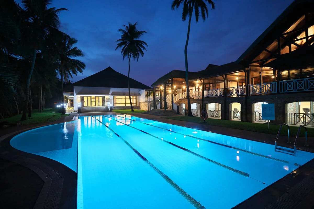 The lap pool and a lit veranda wing of Labadi Beach Hotel at dusk